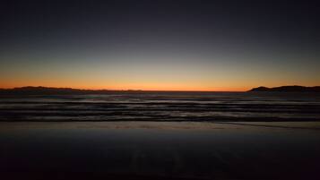 Una spiaggia al tramonto con onde e montagne in lontananza.