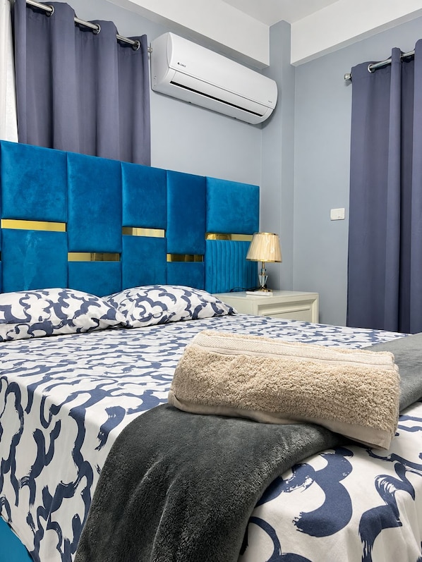 Et hotelværelse med seng, natbord, lampe og en aircondition.