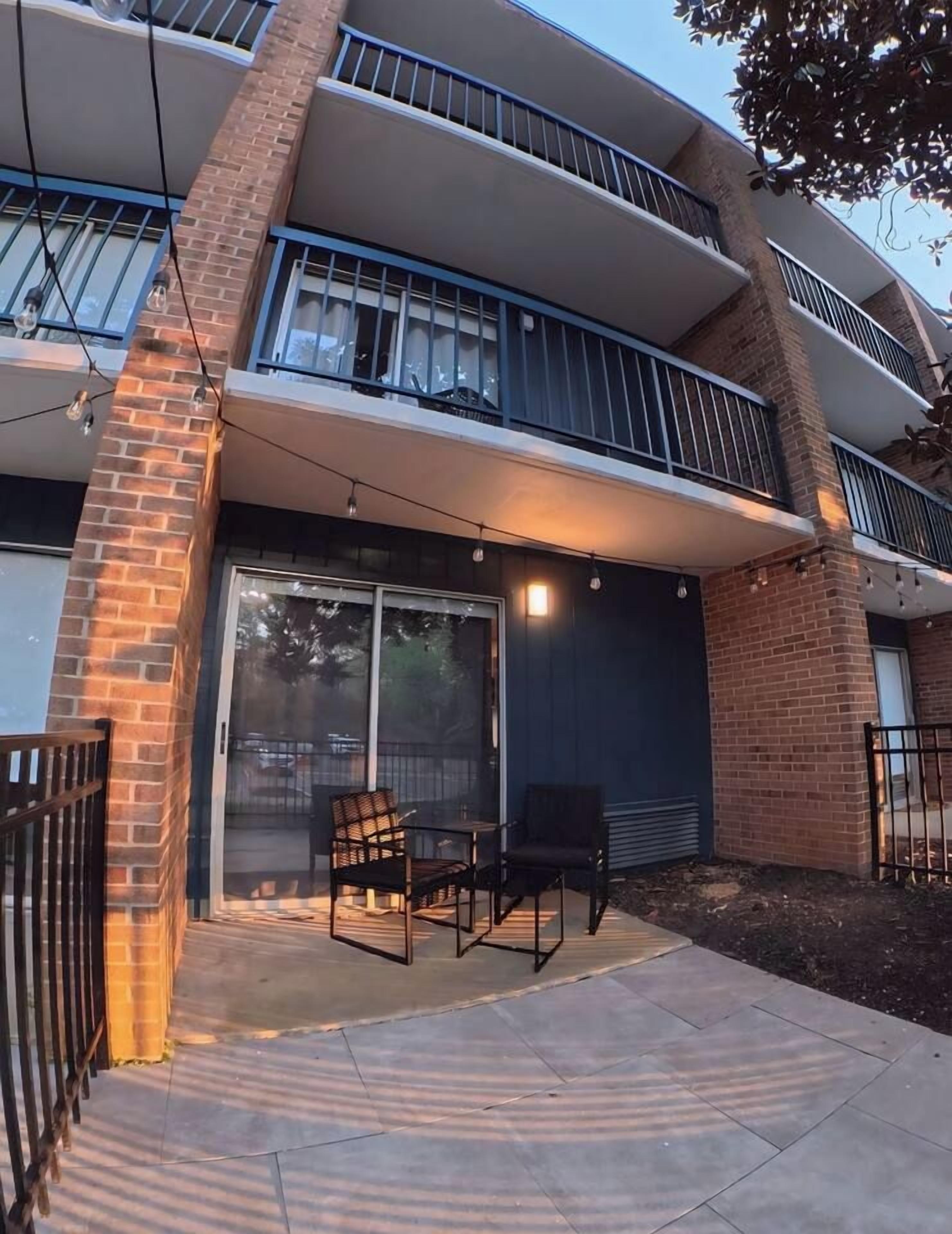 A modern building with a brick facade, large windows, and a balcony with outdoor seating.