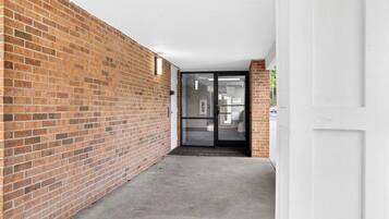 A corridor with a brick wall, a glass door, and a concrete floor.