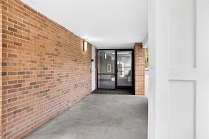 A corridor with a brick wall, a glass door, and a concrete floor. - Work & Relax • Cozy Raleigh Studio (Raleigh)