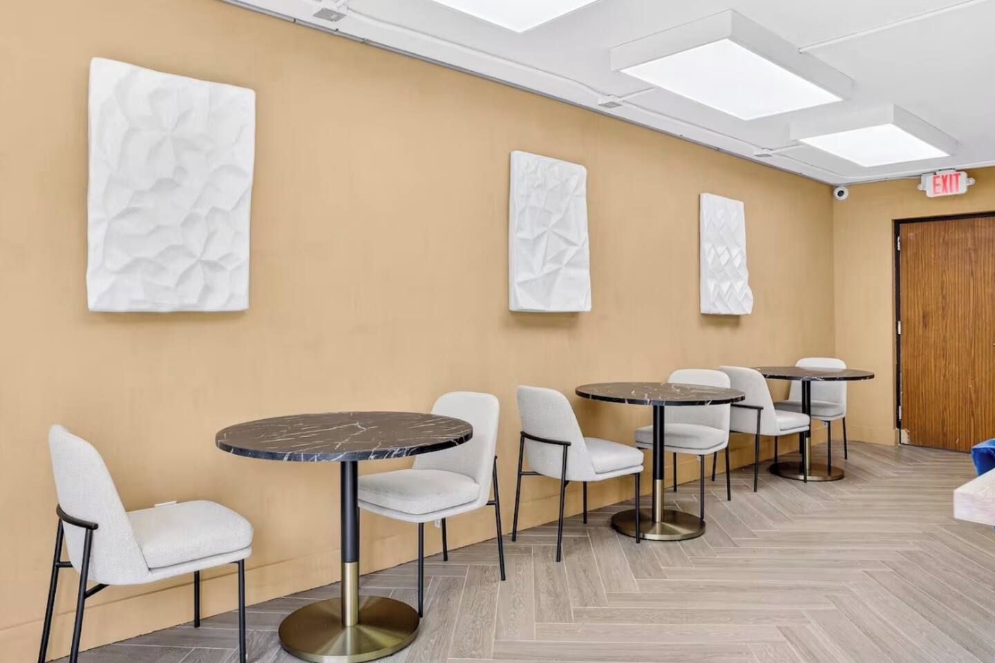 A hotel room with a wooden door, a round table with a marble top, and a seating area with white chairs.