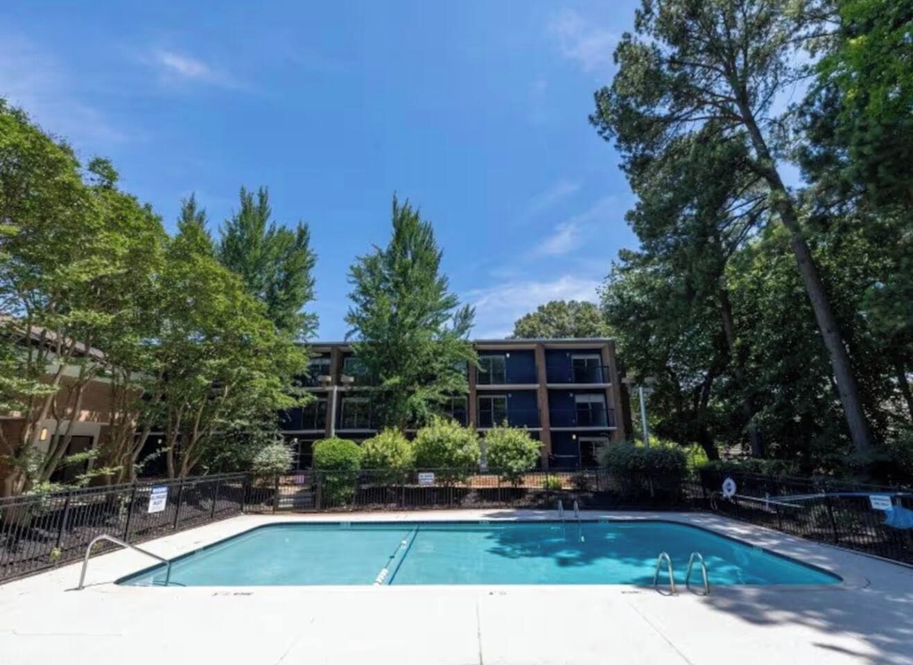 A swimming pool surrounded by trees and a building with multiple windows.