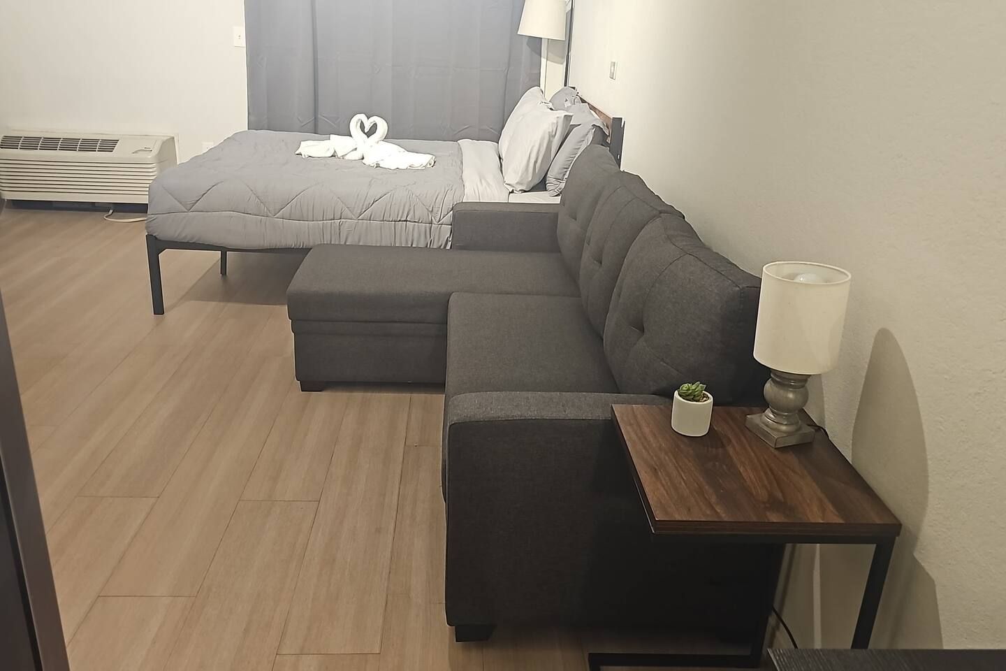A hotel room with a bed, a sofa, a small table with a lamp, and a potted plant.