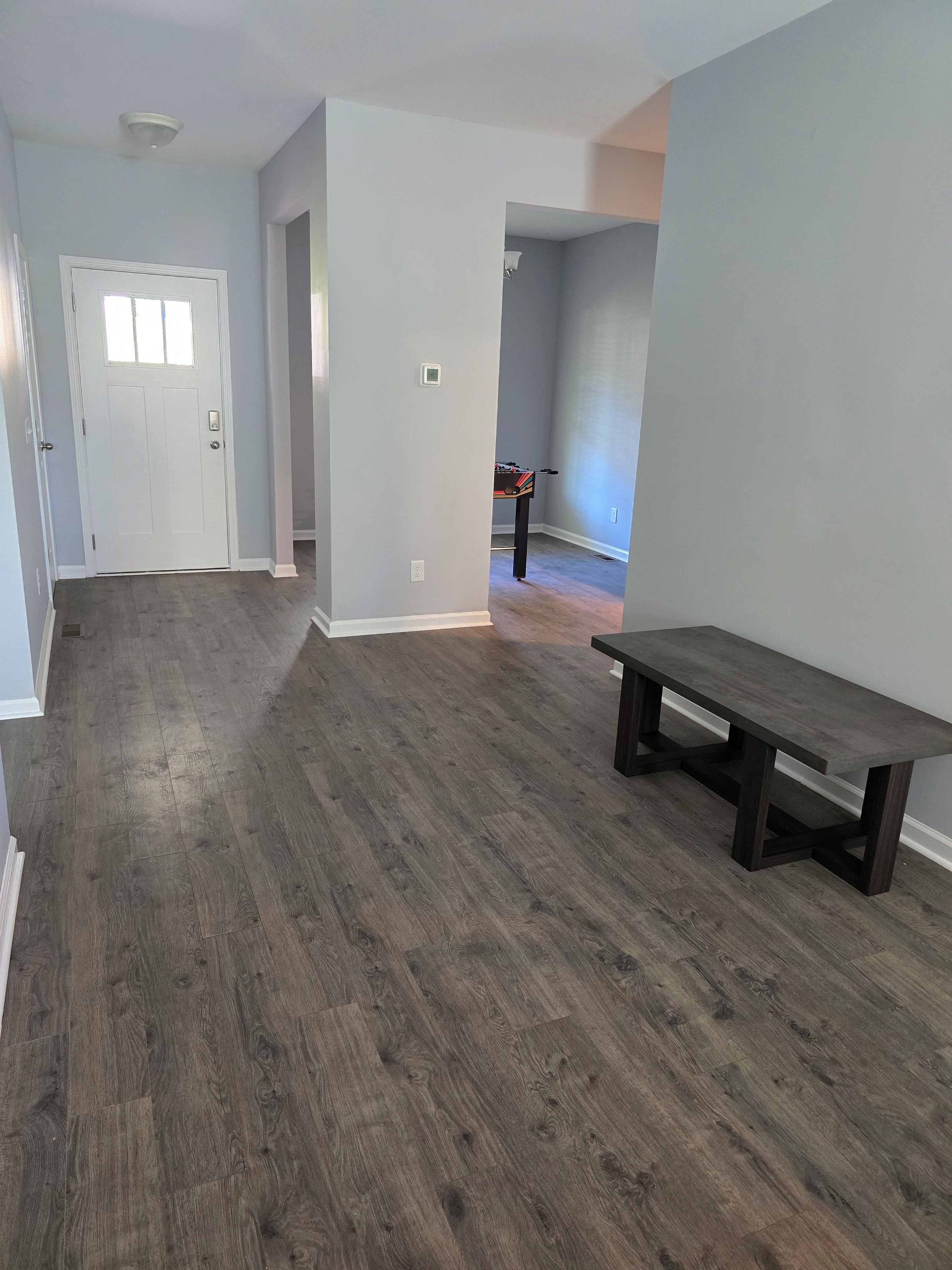 Een ruime kamer met een houten vloer, een bankje en een deur naar een andere kamer.