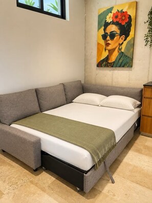 Ein Zimmer mit einem Bett, einem grauen Sofa, einer grünen Decke und einem Bild an der Wand.