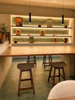 Eine moderne Küche mit einer langen Holzauskleidetheke, drei Barhocker und einem Wandregal mit gerahmten Bildern und Dekoration.