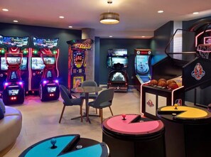 Et område med gaming og flere arkademaskiner, en basketballkurv og siddepladser.