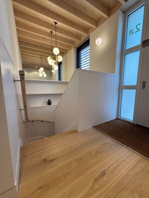 Eine Holztreppe mit Geländer, eine Zwischenebene mit einem kleinen Tisch und einer Vase sowie eine Tür mit Fenster.