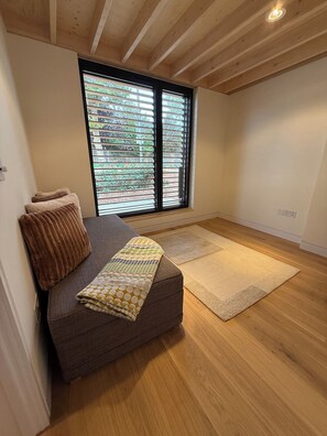 Ein Zimmer mit einer Couch, einer gemusterten Tagesdecke, Holzboden und einem Fenster mit Jalousien.