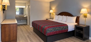 A hotel room with a bed, bedside tables, a nightstand, a wooden cabinet, and a bathroom with a sink and mirror.