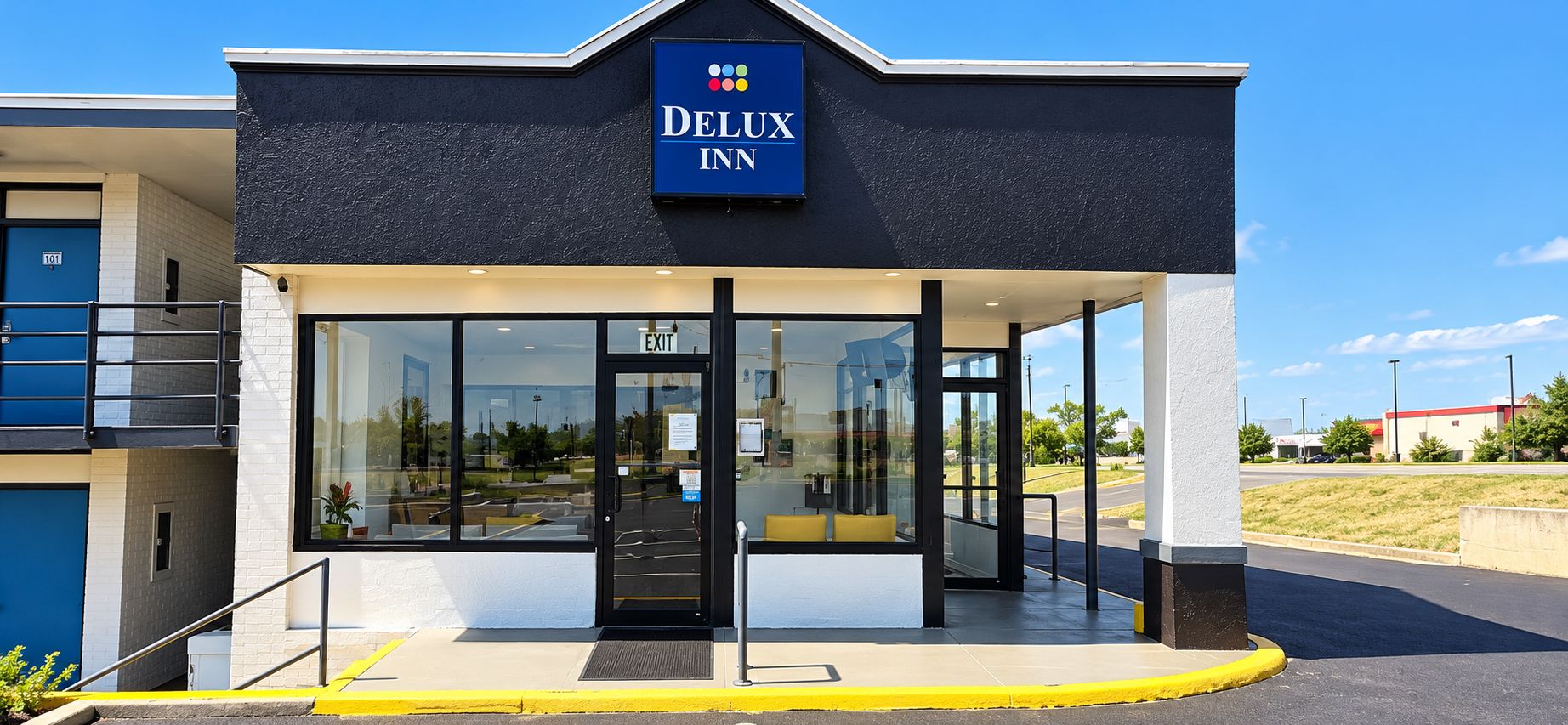 L’entrée d’un hôtel, avec une enseigne indiquant « DELUX INN », et une vue dégagée sur le parking.