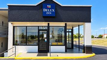 L’entrée d’un hôtel, avec une enseigne indiquant « DELUX INN », et une vue dégagée sur le parking.