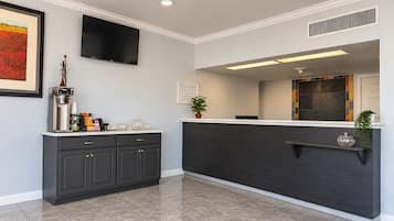 A modern kitchen with dark cabinetry, a countertop, a coffee machine, and a flat-screen TV mounted on the wall.