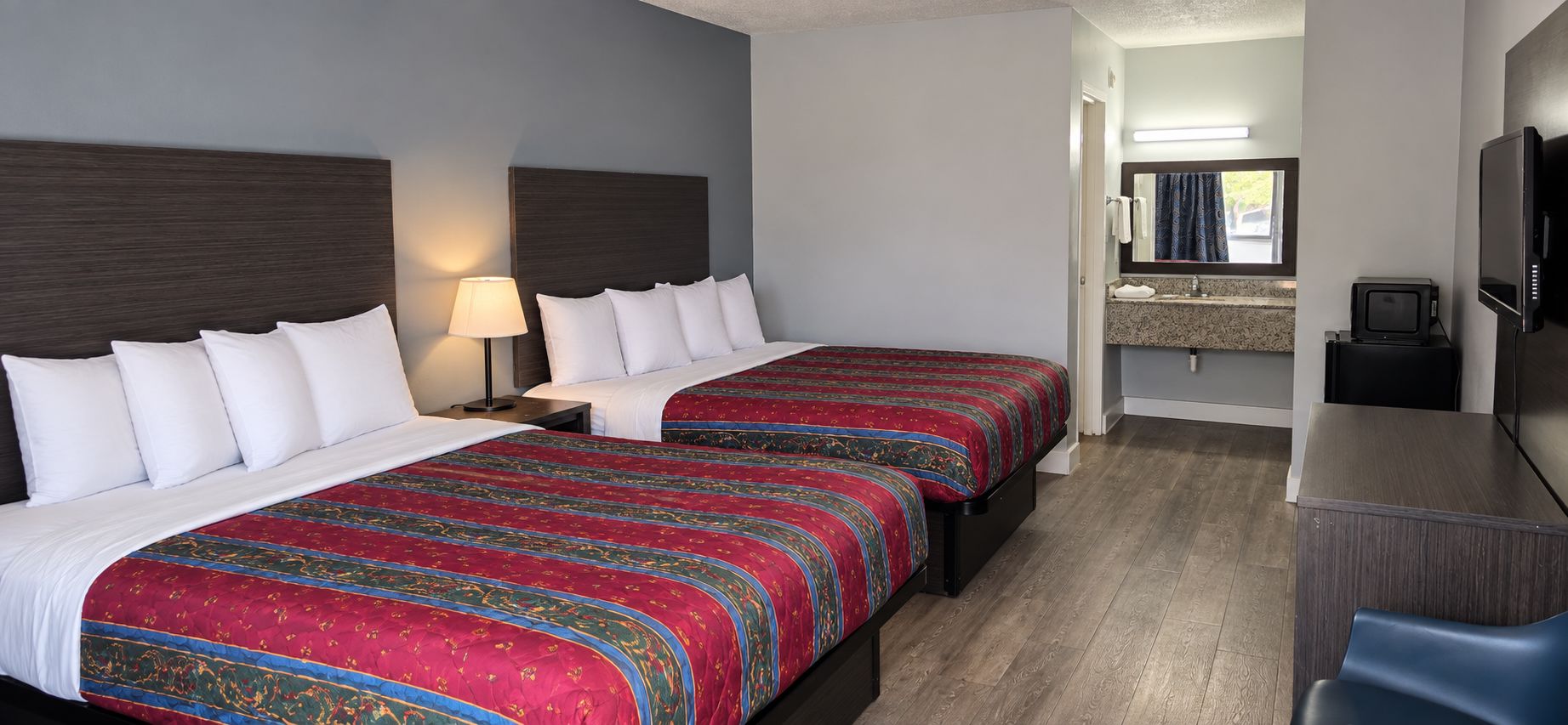 Une chambre d’hôtel avec deux lits, un bureau, une télévision et une salle de bain équipée d’un miroir et d’un lavabo.