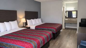 Une chambre d’hôtel avec deux lits, un bureau, une télévision et une salle de bain équipée d’un miroir et d’un lavabo.