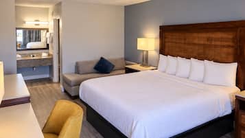 Une chambre d’hôtel avec un grand lit, un canapé, un bureau et une salle de bain visible à travers une porte ouverte.