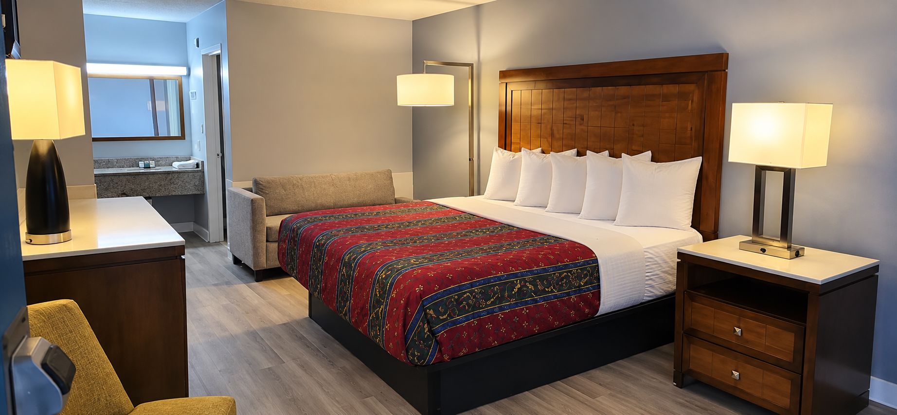 Une chambre d’hôtel comprenant un lit, des tables de chevet, une chaise, un bureau et un miroir.