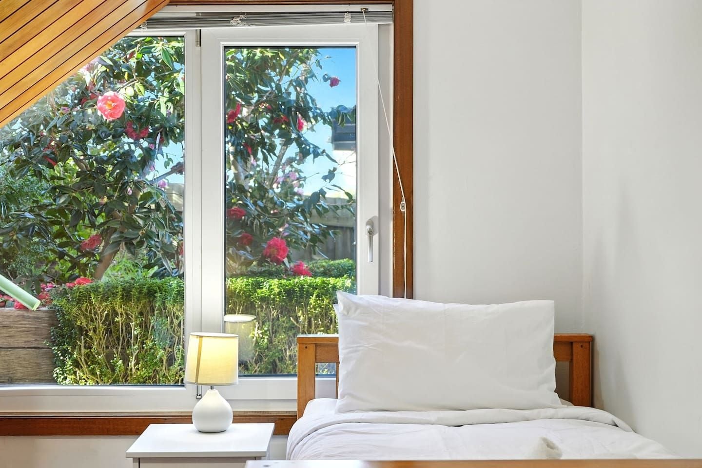 A bedroom with a bed, a bedside table with a lamp, and a window with a view of a garden.