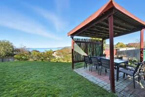Eine überdachte Terrasse im Freien mit Tisch und Stühlen, einem Holzzaun und einem Rasen.