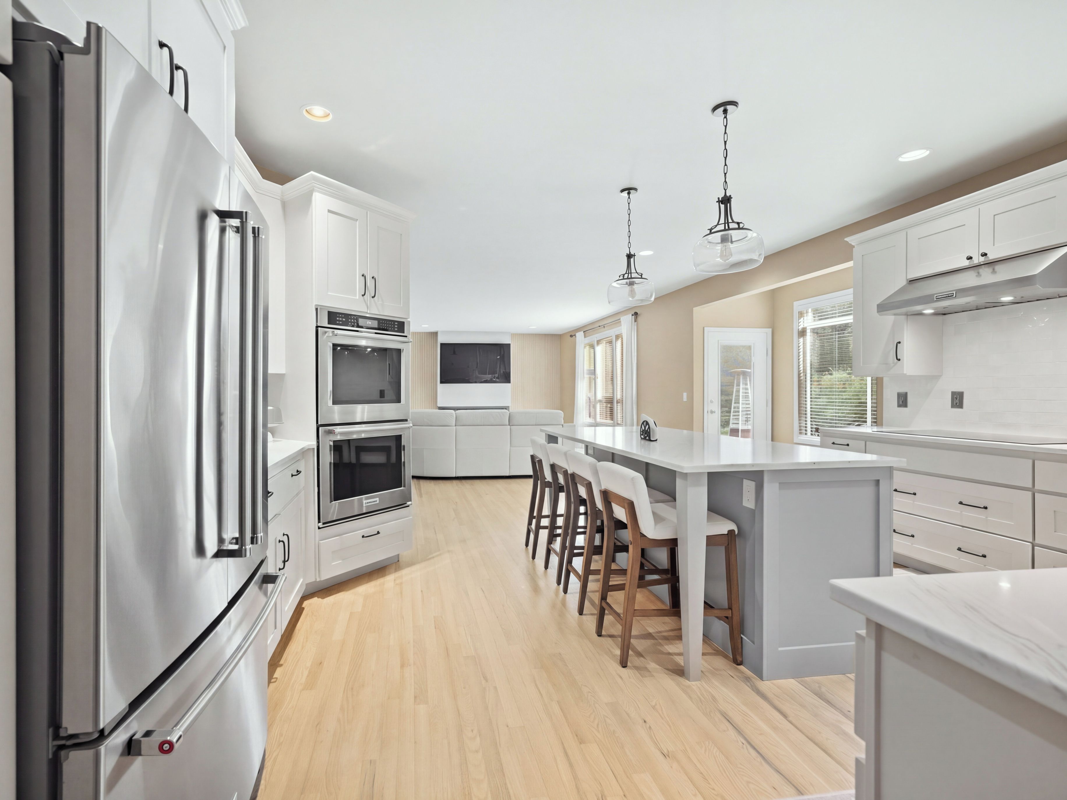 A modern kitchen with white cabinetry, stainless steel appliances, a central island with bar stools, and pendant lighting.