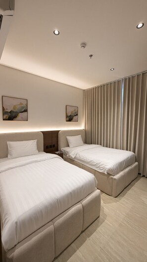 Quarto de hotel com duas camas, uma janela grande com cortinas e obras de arte nas paredes.