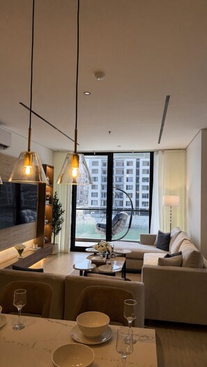 Ein modernes Wohnzimmer mit einer Couch, einem Esstisch und Stühlen. Ein großes Fenster bietet Blick auf Gebäude.