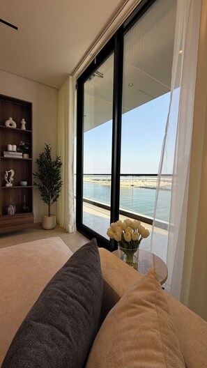 Ein modernes Wohnzimmer mit großem Fenster und Blick auf ein Gewässer, einem Bücherregal und einem Blumentopf.