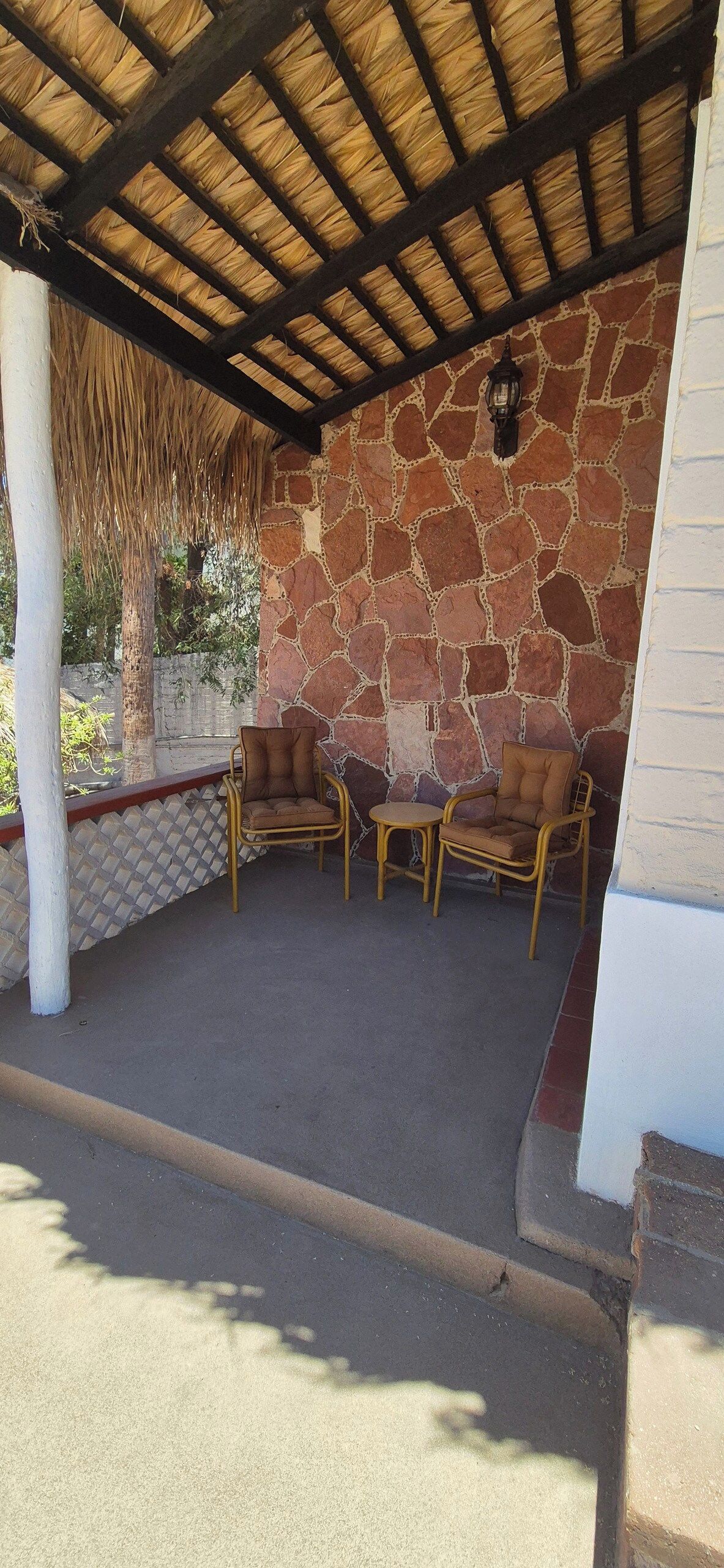 Un patio exterior con paredes de piedra, techo de paja y mobiliario de mimbre.