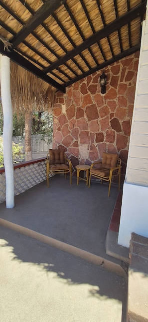 Um pátio externo com paredes de pedra, teto de palha e móveis de vime.