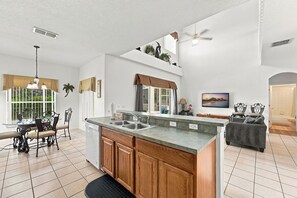 A spacious kitchen with a central island, a dining area with a glass table, and a living room with a sofa and TV. - 5BR Splash House in Davenport | Pool & Game Room (Davenport)