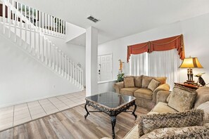 A living room with a staircase, a sofa set, a glass coffee table, and a lamp. - 5BR Splash House in Davenport | Pool & Game Room (Davenport)