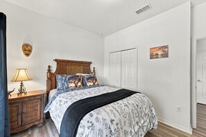 Een slaapkamer met een houten bedframe, een nachtkastje met een lamp, een wandmontage hoofdbord en een deur met een schilderij.
