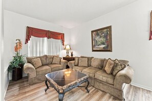 A living room with a sectional sofa, a glass coffee table, a lamp, and a painting on the wall. - 5BR Splash House in Davenport | Pool & Game Room (Davenport)