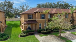 A two-story residential building with a brown roof, a front porch, and a well-maintained lawn. - Regal Palms Haven | 4BR/3.5BA Davenport Resort Townhome with Pool (Davenport)