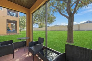 Eine Terrasse mit Korbmöbeln, einem Glastisch und Blick auf eine Rasenfläche und einen Baum.