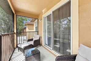 Un balcón con mobiliario de mimbre, una mesa de vidrio y vistas a una zona residencial.