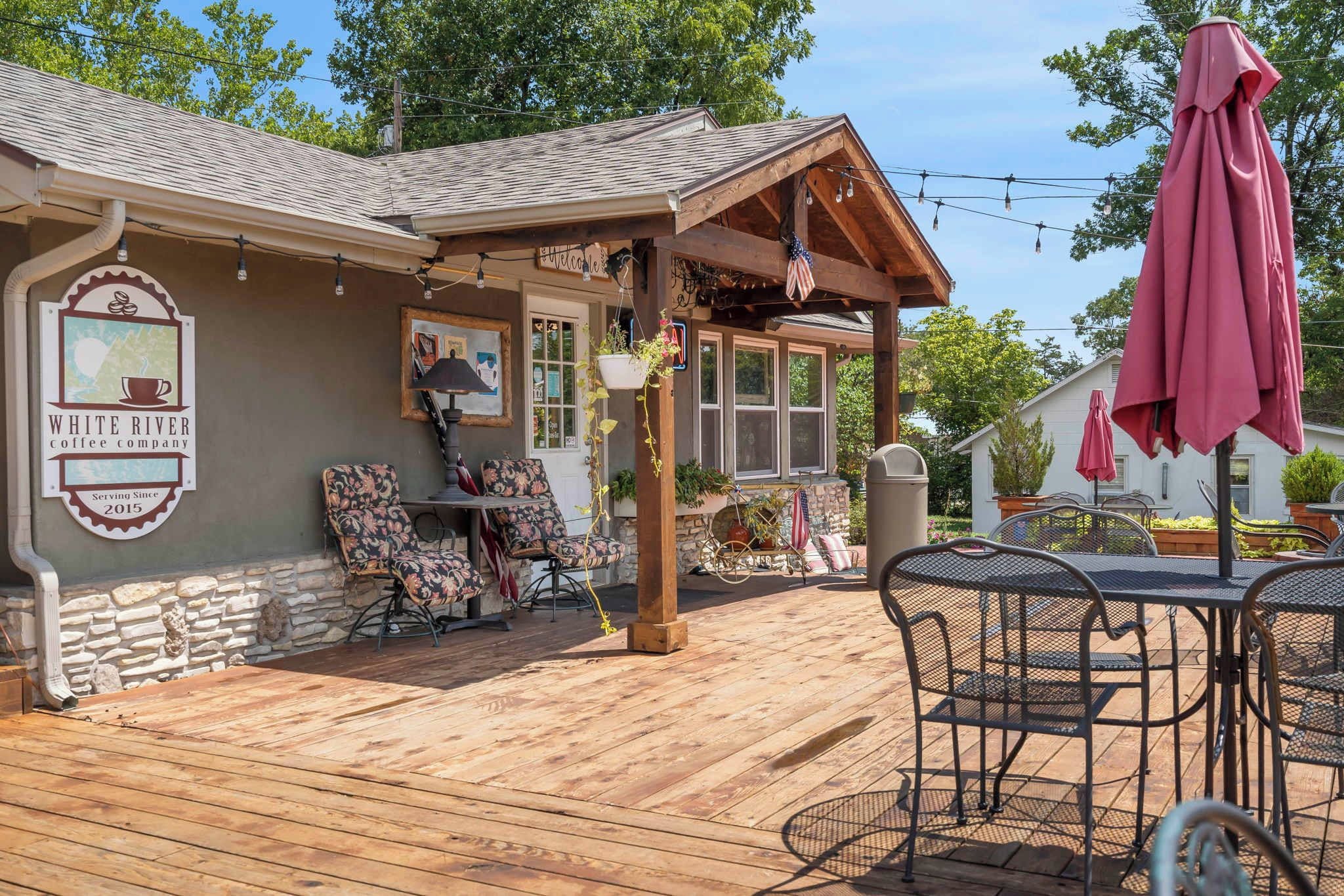 Une terrasse en bois avec des sièges extérieurs, une enseigne indiquant la présence d’un café, et une entrée accueillante.