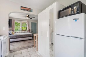A compact room with a bed, a kitchenette with a refrigerator and microwave, a ceiling fan, and a window with curtains. - Heron's Lakeview Hideaway-Walk to the Park/Fishing/Boating/Lake Taneycomo (Rockaway Beach)