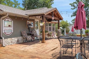 Eine Holzterrasse mit Außenmöbeln, ein Caféschild und ein überdachter Patio-Bereich.