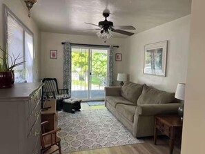 A living room with a sofa, a coffee table, a ceiling fan, and a view through a glass door to the outside. - The Funky Flamingo Lake Retreat-Walk to the Park/Fishing/Boating (Rockaway Beach)