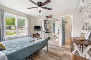 Un dormitorio con cama, ventilador de techo, televisor y ventana con vistas al exterior.