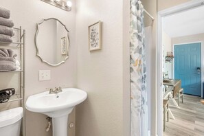 Un baño con lavamanos blanco, un espejo, toallero y cortina de ducha.