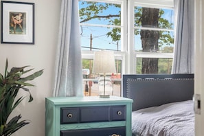Une chambre à coucher avec un lit, une table de chevet avec une lampe, un tableau encadré et une fenêtre avec des rideaux.