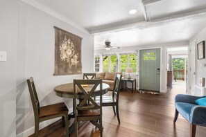 A dining area with a round table and chairs, a ceiling fan, and a view of the outdoors through large windows. - The Ravens Roost Lakeview Retreat-Walk to the Park/Fishing/Boating (Rockaway Beach)