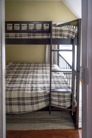 Un letto a castello con copripiumino a quadri in una stanza con pavimento in legno e parete spoglia.
