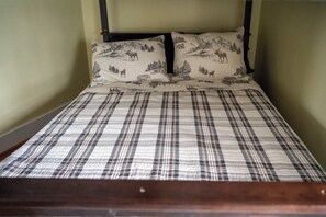 Un letto con una coperta a quadri e due cuscini con un motivo naturalistico.