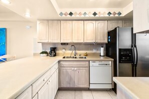 A modern kitchen with light wood cabinets, stainless steel appliances, and a dishwasher. - Wake Up to the Atlantic: On-the-Beach Cocoa Beach Condo w/ Heated Pool & Beach Gear (Cocoa Beach)