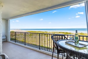 Un balcón con vista a la playa, una mesa con una botella y una silla.