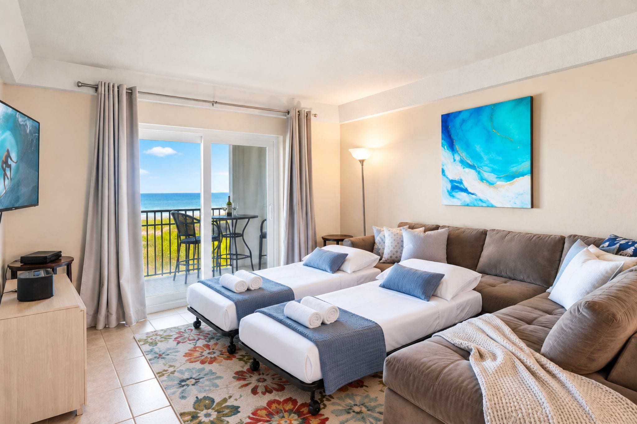 Une chambre d’hôtel avec deux lits, un canapé, une télévision, un bureau et un balcon avec vue sur la mer.